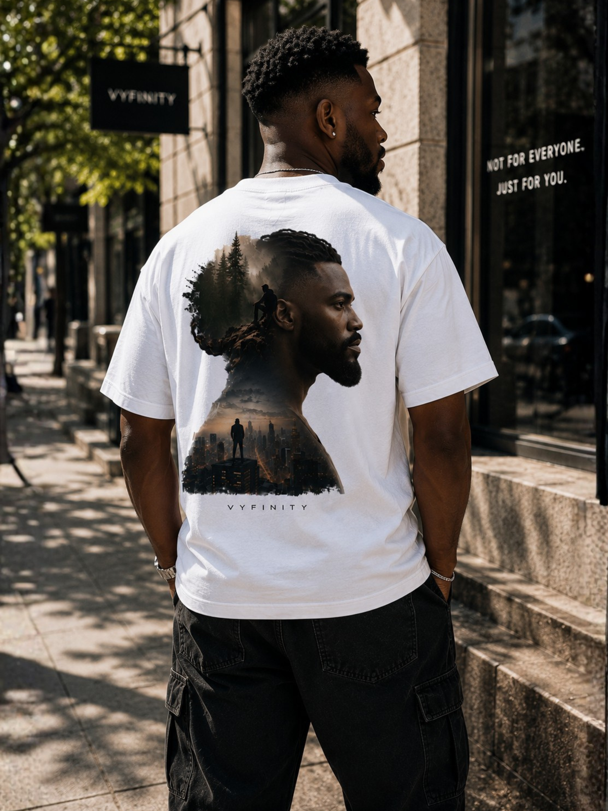 Männliches Model trägt ein weißes VYFINITY Heavy T-Shirt in Rückansicht. Großer Double-Exposure-Rückenprint mit männlichem Seitenprofil, Waldlandschaft, einsamer Figur und urbaner Skyline. Streetwear-Lifestyle-Aufnahme in moderner Innenstadt.