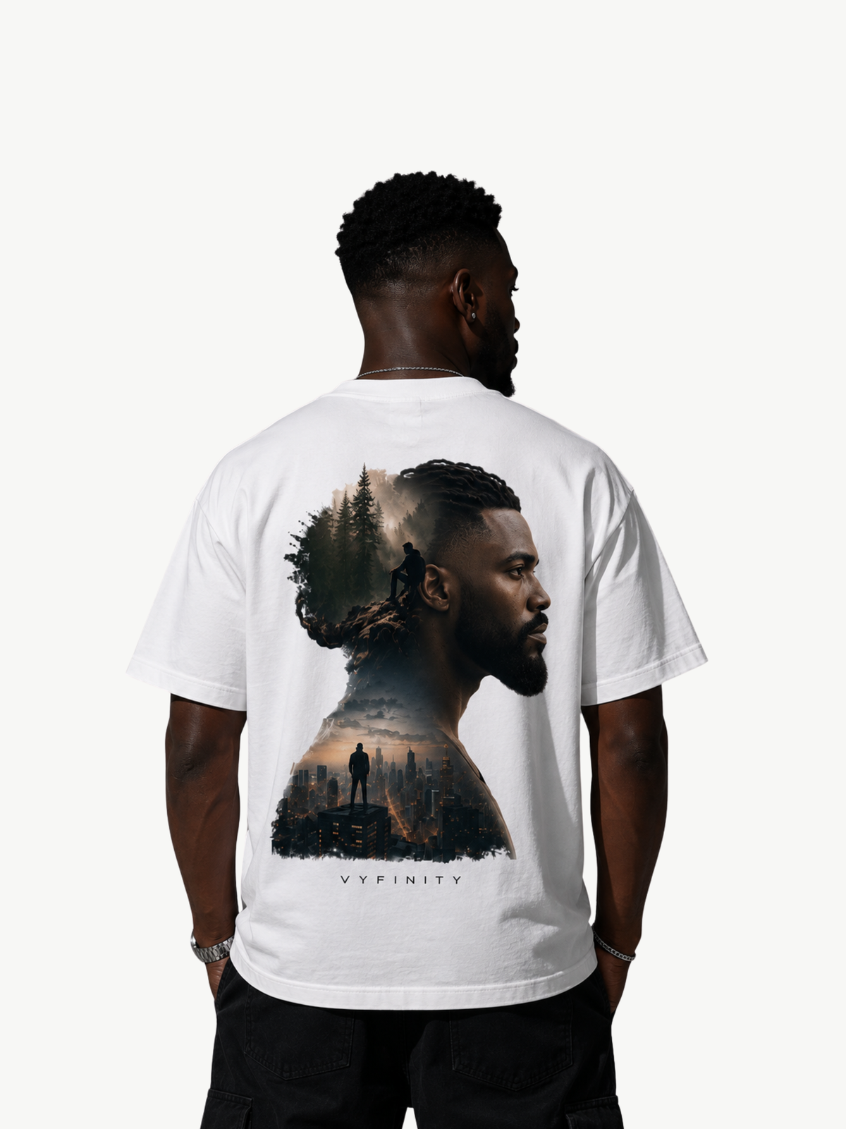 Männliches Model trägt ein weißes VYFINITY Heavy T-Shirt in Rückansicht. Großflächiger Double-Exposure-Rückenprint mit männlichem Seitenprofil, Waldlandschaft, einsamer Figur und urbaner Skyline. Studioaufnahme vor weißem Hintergrund.