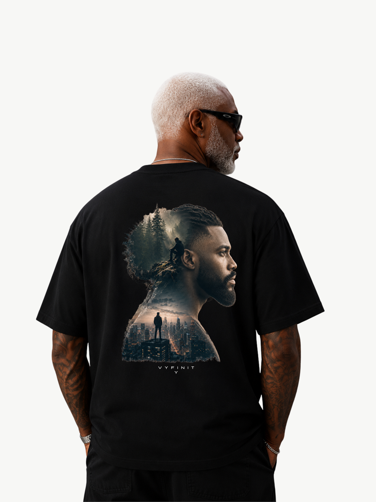 Männliches Model trägt ein schwarzes VYFINITY Heavy T-Shirt mit großem künstlerischem Rückenprint. Das Motiv zeigt ein männliches Seitenprofil als Doppelbelichtung mit Waldlandschaft und urbaner Skyline. Studioaufnahme vor hellem Hintergrund.