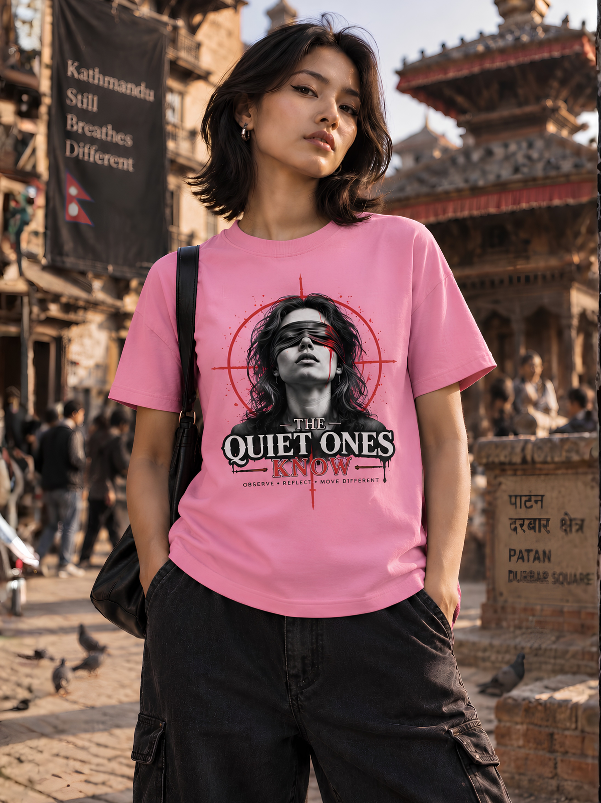 Nepalesisches weibliches Model trägt ein rosa VYFINITY Regular Fit T-Shirt mit großem „THE QUIET ONES KNOW“-Print in Schwarz, Weiß und Rot. Lifestyle-Aufnahme auf einem historischen Platz in Kathmandu, Nepal.
