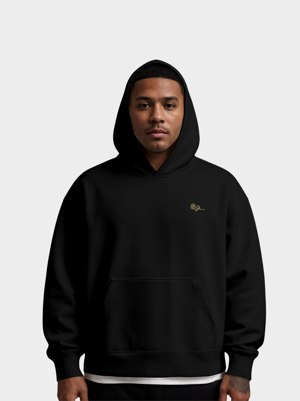 Schwarzer Hoodie mit kleiner goldener Rose auf der linken Brust, getragen von einem Model. Minimalistisches Design mit Kapuze und Fronttasche, modernes Streetwear-Piece für einen edlen Look.