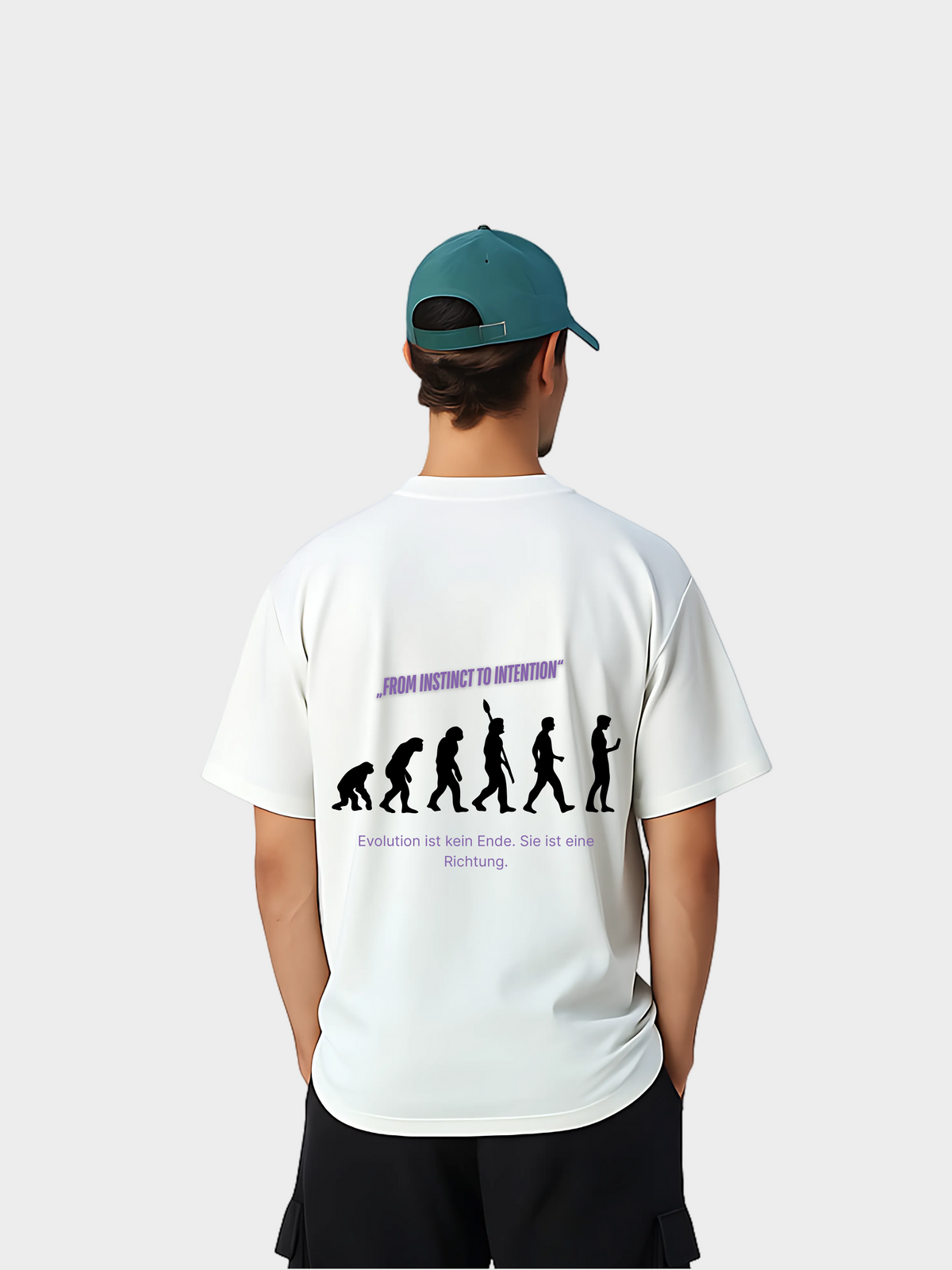 Oversized T-Shirt in Weiß mit großem Evolution-Print auf dem Rücken. Schwarze Silhouetten zeigen die Entwicklung vom Affen bis zum modernen Menschen, ergänzt durch den Text „FROM INSTINCT TO INTENTION“ und „Evolution ist kein Ende. Sie ist eine Richtung.“ Streetwear-Style mit Message, getragen von einem Model mit grüner Cap.