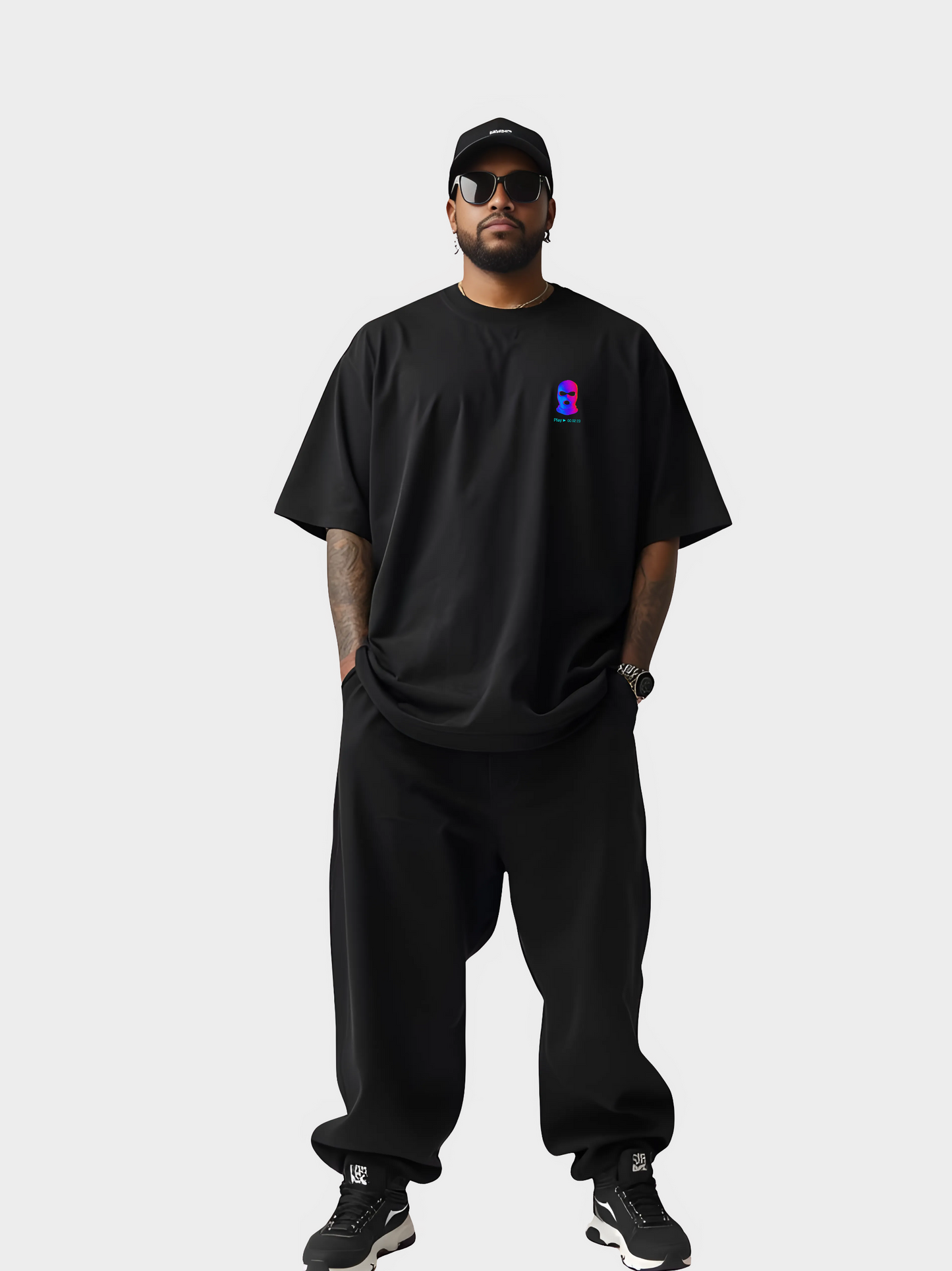 Vyfinity City Noise T-Shirt in Schwarz, Oversized Fit, getragen von einem Model in kompletter Streetwear-Ansicht. Schwarze Cap, Sonnenbrille, weite Hose und Sneaker. Brustprint mit bunter Maske im VHS-Style.