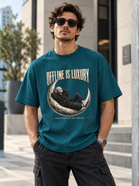 Petrol-/Teal-farbenes Oversized Heavy T-Shirt mit großem „OFFLINE IS LUXURY“-Frontprint. Zentral liegt eine entspannte Alien-Figur im schwarzen Hoodie mit Kopfhörern auf einer detailreichen Mondsichel. Darunter „DISCONNECTED BY CHOICE“. Moderner Premium-Streetwear-Look mit starkem Creme-, Schwarz- und Grau-Kontrast auf Petrol.
