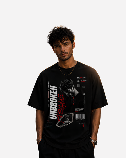 Junger Mann trägt ein schwarzes Vyfinity Oversized T-Shirt mit dem „Unbroken“ Frontprint. Das grafische Streetwear-Design kombiniert ein monochromes Porträt, rote Typografie, Barcode, technische Elemente und motivierende Botschaften im modernen Urban-Style. Premium Baumwollshirt für Damen und Herren mit lockerem Oversized Fit.