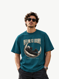 Männliches Model mit Sonnenbrille trägt ein petrolfarbenes Oversized VYFINITY T-Shirt mit großem „OFFLINE IS LUXURY“-Frontprint. Das Motiv zeigt eine entspannte Figur mit Kopfhörern auf einer Mondsichel und den Schriftzug „DISCONNECTED BY CHOICE“. Modernes Streetwear-Outfit mit cleanem Hintergrund.