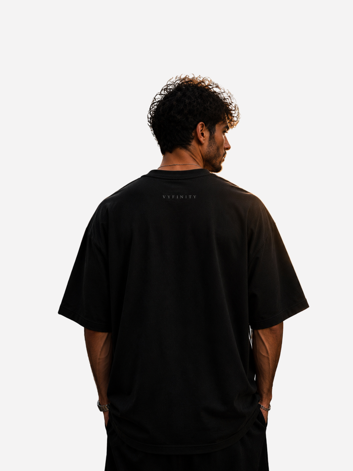 Junger Mann trägt die Rückseite eines schwarzen Vyfinity Oversized T-Shirts aus hochwertiger Baumwolle. Das minimalistische Streetwear-Shirt besitzt ein dezentes Vyfinity-Logo im Nackenbereich und einen modernen Oversized Fit. Cleanes Premium Fashion-Design für Damen und Herren im Urban- und Luxury-Streetwear-Stil.