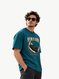 Männliches Model mit Sonnenbrille trägt ein petrolfarbenes Oversized T-Shirt mit großem „OFFLINE IS LUXURY“-Frontprint. Das Motiv zeigt eine entspannte Alien-Figur im Hoodie mit Kopfhörern auf einer Mondsichel. Darunter steht „DISCONNECTED BY CHOICE“. Moderner VYFINITY Streetwear-Look.