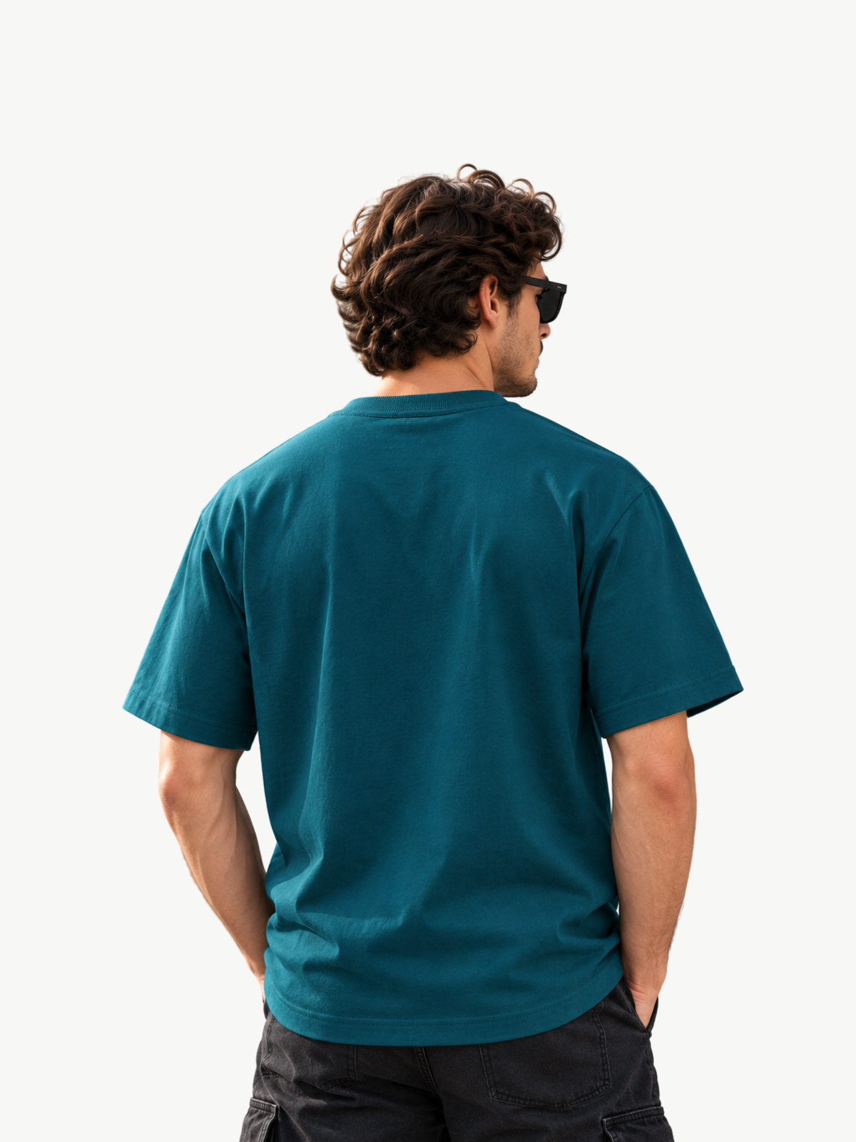 Männliches Model mit Sonnenbrille trägt ein petrolfarbenes Oversized T-Shirt in Rückenansicht. Die Rückseite ist bewusst ohne Print oder Logo gehalten. Lockerer Streetwear-Fit mit kurzen Ärmeln, kombiniert mit schwarzer Hose vor cleanem weißem Hintergrund.