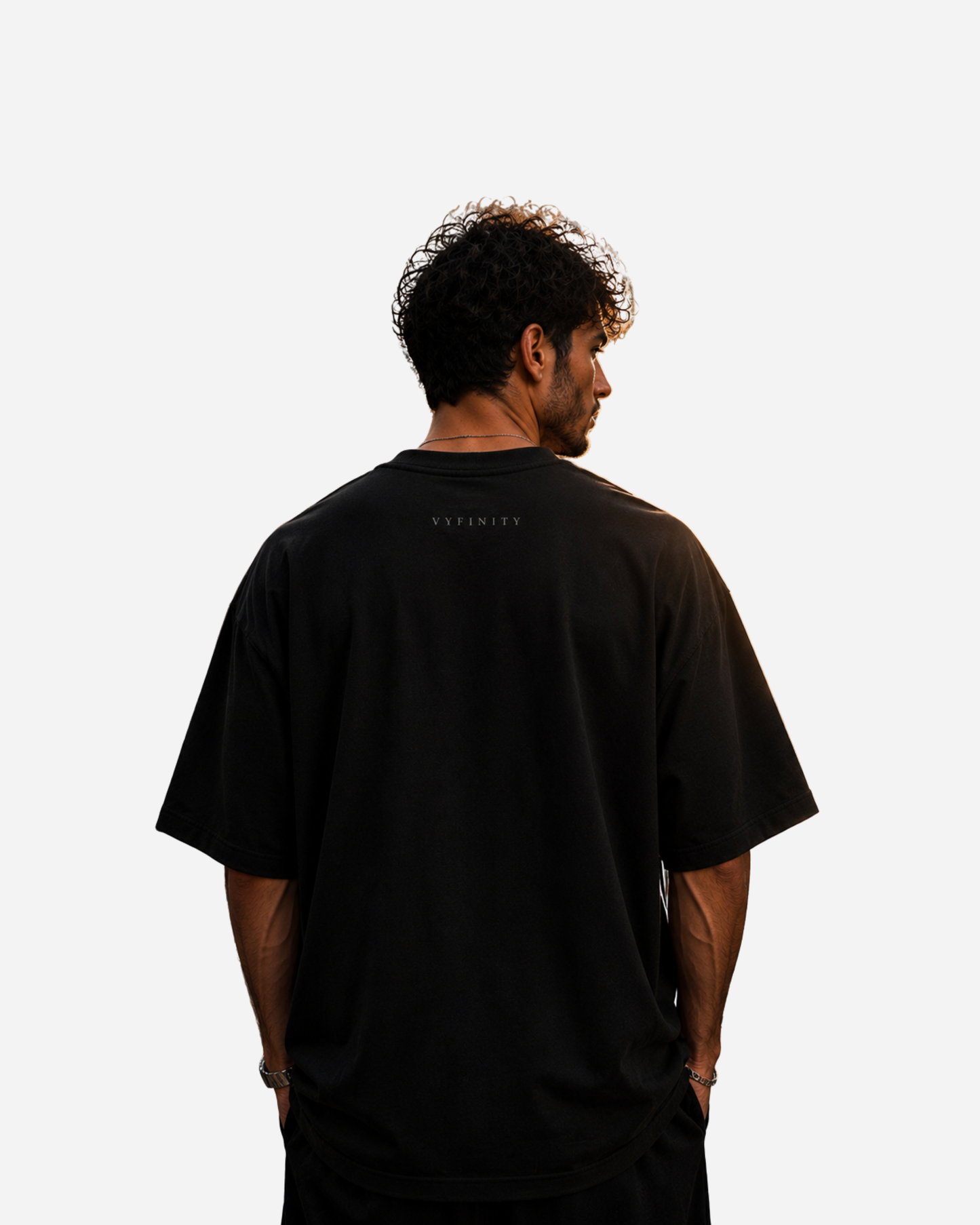 Junger Mann trägt die Rückseite eines schwarzen Vyfinity Oversized T-Shirts aus hochwertiger Baumwolle. Das minimalistische Streetwear-Shirt besitzt ein dezentes Vyfinity-Logo im Nackenbereich und einen modernen Oversized Fit. Cleanes Premium Fashion-Design für Damen und Herren im Urban- und Luxury-Streetwear-Stil.
