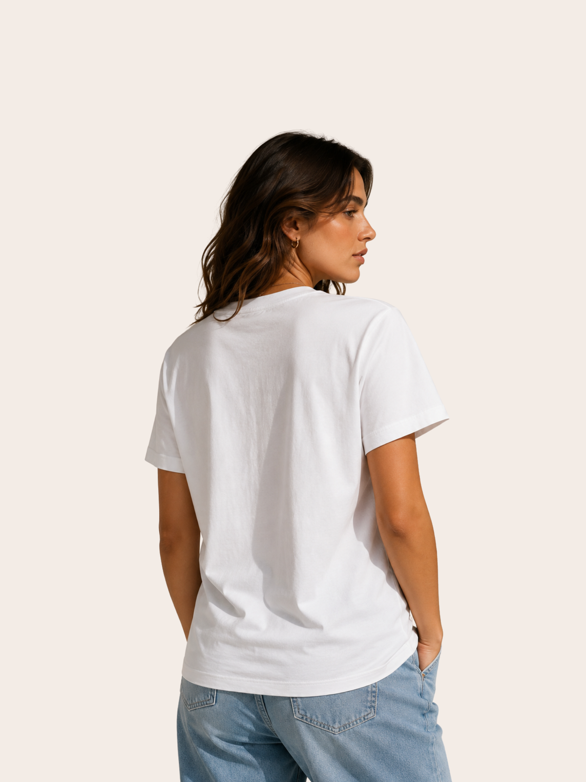 Rückansicht einer Frau in einem schlichten weißen VYFINITY T-Shirt ohne Rückenprint, kombiniert mit hellblauer Jeans. Das Shirt zeigt einen klassischen Rundhalsausschnitt, kurze Ärmel und eine gerade, lockere Passform. Minimalistische Studioaufnahme vor warmem, cremefarbenem Hintergrund.