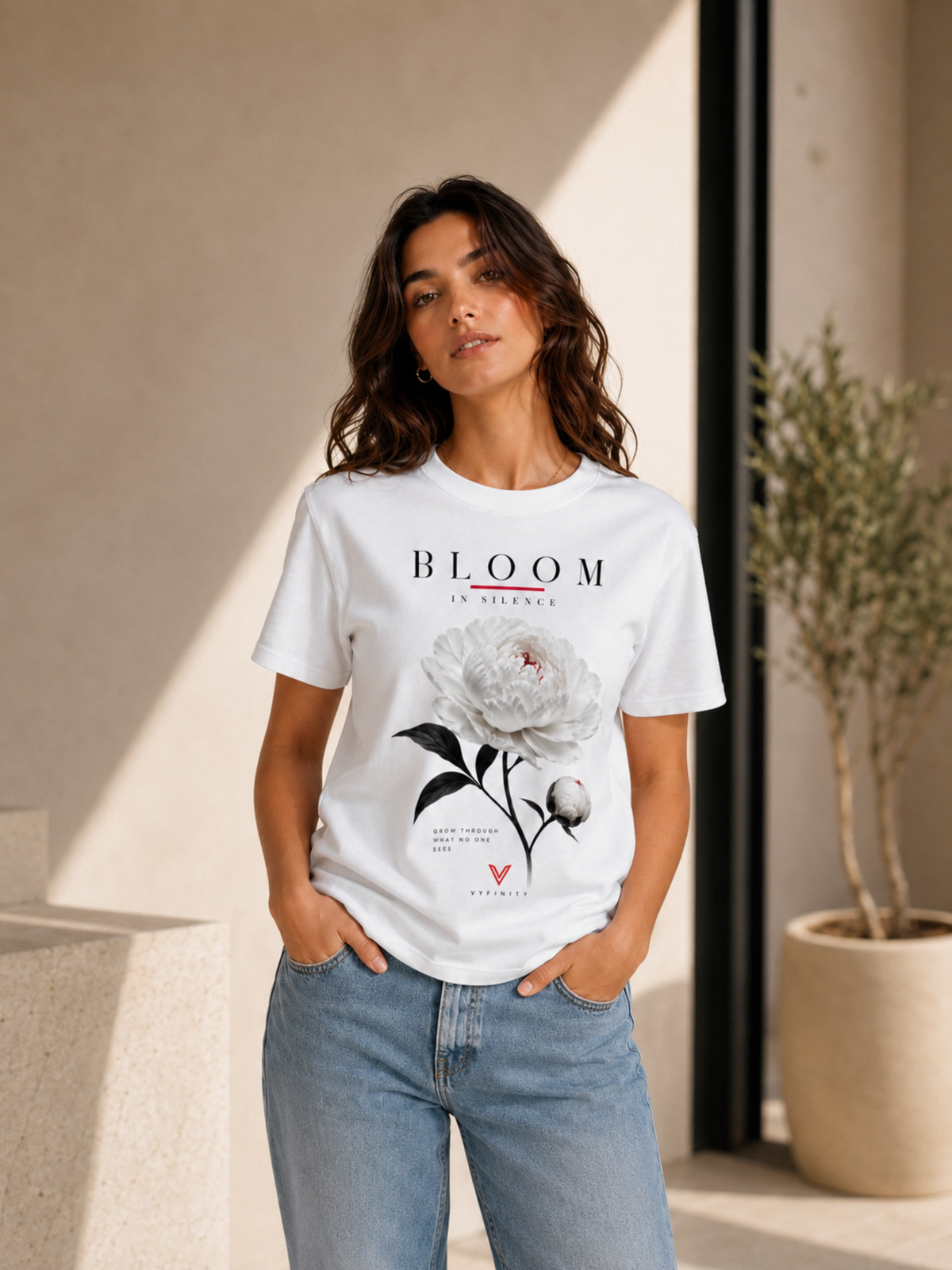Frau trägt ein weißes VYFINITY T-Shirt mit großem „BLOOM IN SILENCE“-Frontprint, weißer Pfingstrose, schwarzen Blättern und roten Akzenten. Das florale Damen-Shirt wird mit hellblauer Jeans in einem modernen, warm beleuchteten Lifestyle-Setting präsentiert.