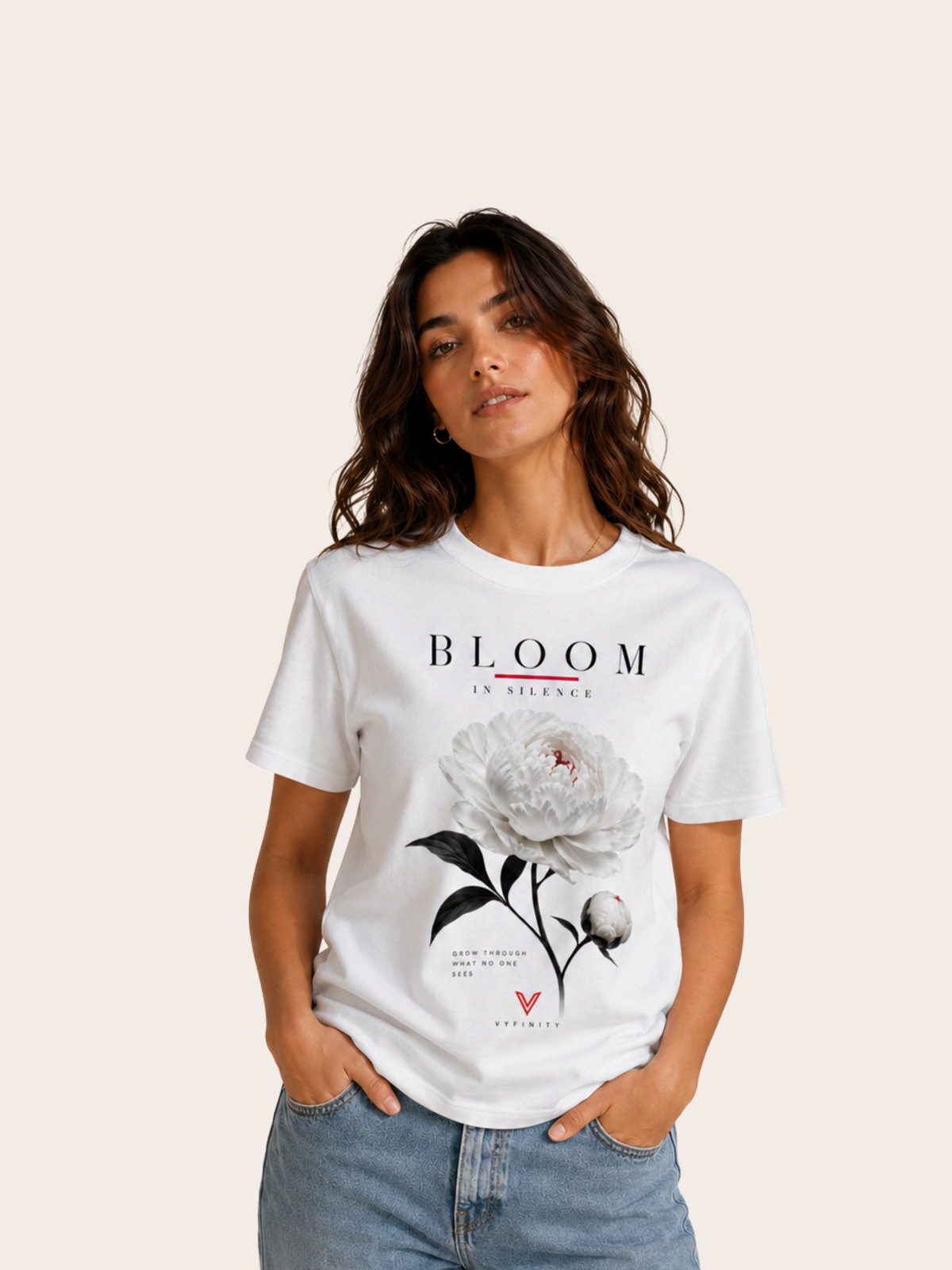 Frau trägt ein weißes VYFINITY T-Shirt mit großem „BLOOM IN SILENCE“-Frontprint. Das florale Design zeigt eine weiße Blüte mit schwarzen Stielen und Blättern, dezenten roten Akzenten sowie VYFINITY-Branding. Kombiniert mit heller Jeans vor einem minimalistischen Studiohintergrund.