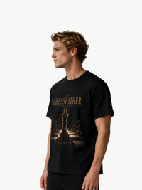 VYFINITY „The Chessfather“ schwarzes T-Shirt für Herren in seitlicher Frontansicht mit goldfarbenem Schach-Design, zentraler Königsschachfigur und Schachbrett-Motiv, getragen von einem männlichen Model vor weißem Hintergrund.