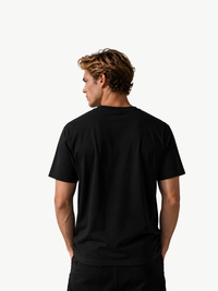 VYFINITY schwarzes Herren-T-Shirt in Rückenansicht, getragen von einem männlichen Model mit blondem Haar vor weißem Hintergrund. Schlichte schwarze Rückseite ohne Print oder sichtbares Design.