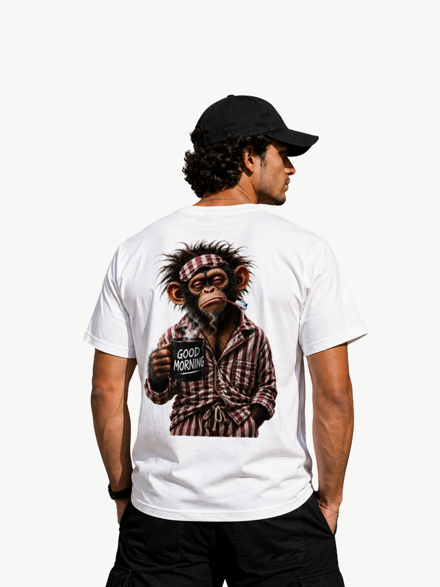 Männliches Model in Rückansicht mit weißem VYFINITY T-Shirt und schwarzer Cap. Großer Rückenprint mit müdem Affen im karierten Pyjama, Zahnbürste und schwarzer „GOOD MORNING“-Kaffeetasse. Heller minimalistischer Hintergrund.