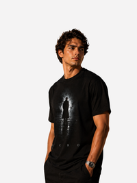Junger Mann trägt schwarzes Vyfinity Classic Fit Unisex T-Shirt mit ECHO Frontprint. Dunkles minimalistisches Streetwear-Design mit geheimnisvoller Silhouette im Nebel und spiegelnder Reflexion – moderner Urban Fashion Lifestyle-Look.