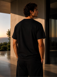 Rückansicht eines jungen Mannes in einem schwarzen Vyfinity Classic Fit Unisex T-Shirt vor einer modernen Luxusvilla. Minimalistisches Premium Baumwoll-Shirt mit cleanem Rücken ohne Print, zeitlosem Streetwear-Design und hochwertigem Urban Fashion Look.
