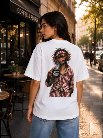 „Frau trägt ein weißes VYFINITY Relaxed Fit T-Shirt mit großem Affen-‚GOOD MORNING‘ Rückenprint vor einem Café in der Stadt bei warmem Abendlicht.“