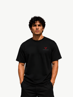 Männliches Model trägt ein schwarzes VYFINITY T-Shirt im Regular Fit mit kleinem rot-weißem VYFINITY Logo auf der linken Brust, kombiniert mit schwarzer Hose vor einem hellen, minimalistischen Hintergrund.