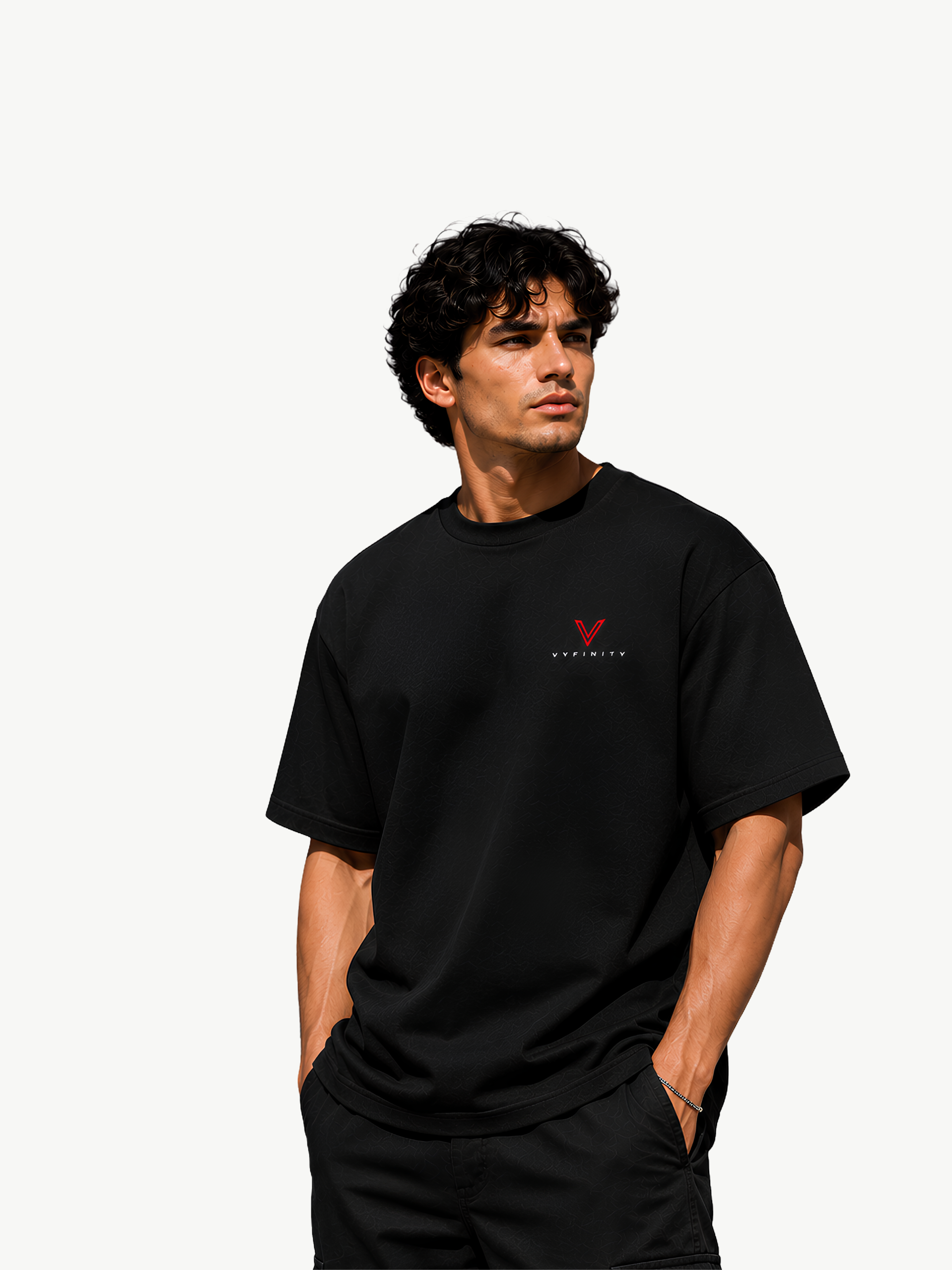 Männliches Model mit dunklen Locken trägt ein schwarzes VYFINITY T-Shirt im Regular Fit mit kleinem rot-weißem VYFINITY Logo auf der linken Brust, kombiniert mit schwarzer Hose vor hellem, minimalistischem Hintergrund.