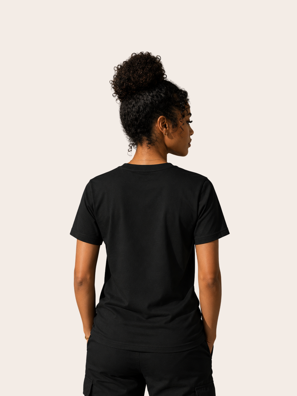 Frau von hinten in einem schwarzen VYFINITY T-Shirt ohne Rückenprint. Das schlichte schwarze Shirt wird mit schwarzer Hose kombiniert und in einer cleanen Studioaufnahme vor hellem, cremefarbenem Hintergrund präsentiert.