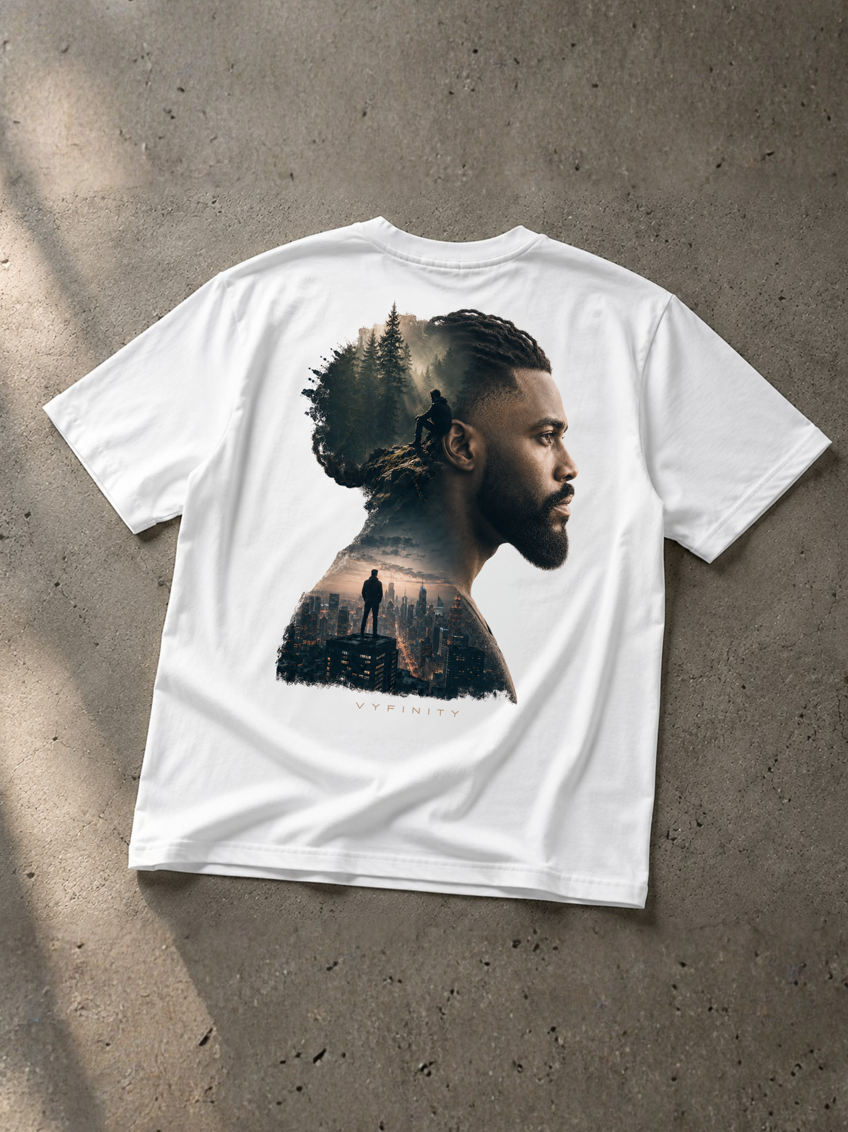 Weißes VYFINITY Heavy T-Shirt als Flatlay auf grauem Betonboden. Die Rückseite zeigt einen großen Double-Exposure-Print mit dem Seitenprofil eines Mannes, dunklem Wald, einzelnen Silhouetten und urbaner Skyline. Dezenter VYFINITY-Schriftzug unter dem Motiv. Natürliches Licht betont Stoff und Druckdetails.