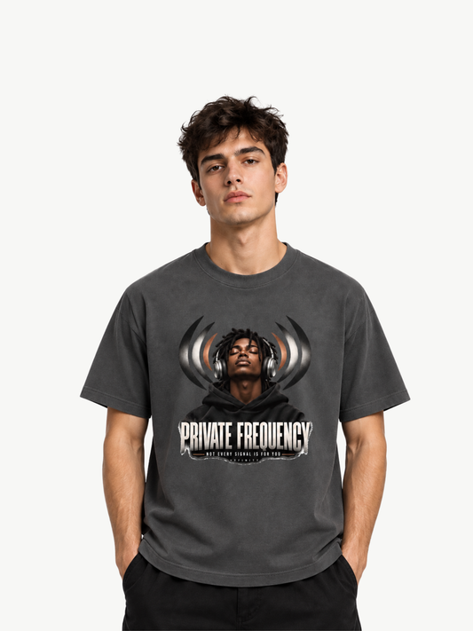Anthrazitfarbenes Regular-Fit T-Shirt, 180 GSM, mit großem Frontprint „PRIVATE FREQUENCY“. Zentrales Motiv: schwarzer Mann im schwarzen Hoodie mit großen Over-Ear-Kopfhörern und geschlossenen Augen; dahinter stilisierte Schallwellen in Schwarz, Grau und warmen Kupferakzenten. Darunter der Schriftzug „NOT EVERY SIGNAL IS FOR YOU“ sowie dezentes VYFINITY-Branding. Moderner urbaner Streetwear-Look. Rückseite ohne Print.