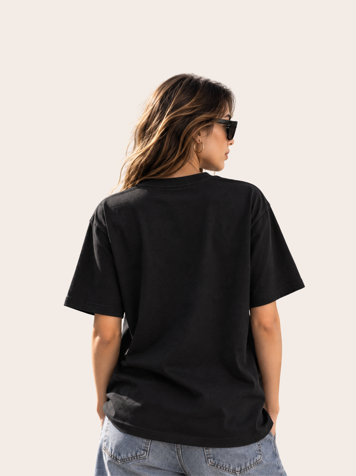 Rückansicht einer Frau mit schwarzem Oversized Heavy T-Shirt. Die Rückseite des Shirts ist komplett clean und ohne Print, Logo oder Schriftzug. Lockerer moderner Streetwear-Fit mit überschnittenen Schultern und weiten Ärmeln, kombiniert mit heller Cargo-/Denim-Hose und schwarzer Sonnenbrille.