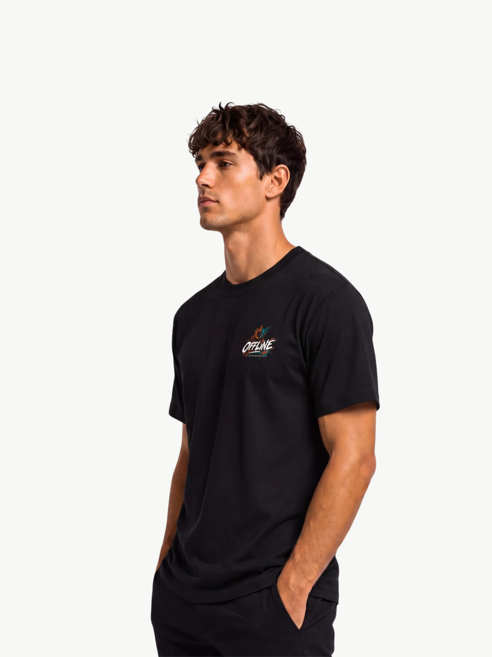 Männliches Model trägt ein schwarzes VYFINITY T-Shirt mit kleinem farbigen „OFFLINE“-Design auf der linken Brust. Seitliche Dreiviertelansicht mit einer Hand in der Hosentasche vor weißem Studiohintergrund.