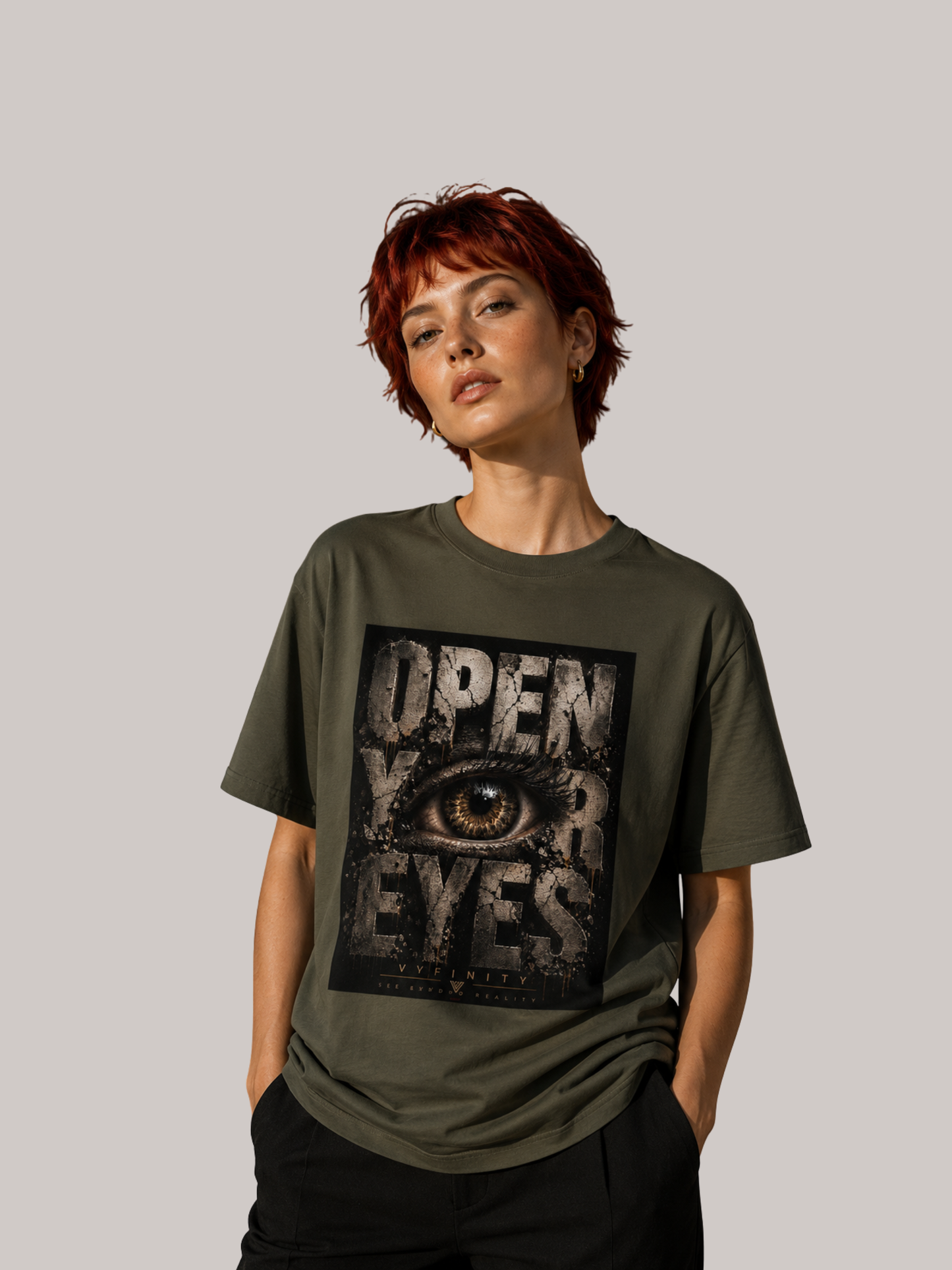 Junge Frau mit kurzen roten Haaren trägt ein olivgrünes VYFINITY Unisex T-Shirt mit großem „OPEN YOUR EYES“-Print und realistischem Auge im markanten Grunge-Design. Moderner Streetwear-Look vor neutralem Studiohintergrund.
