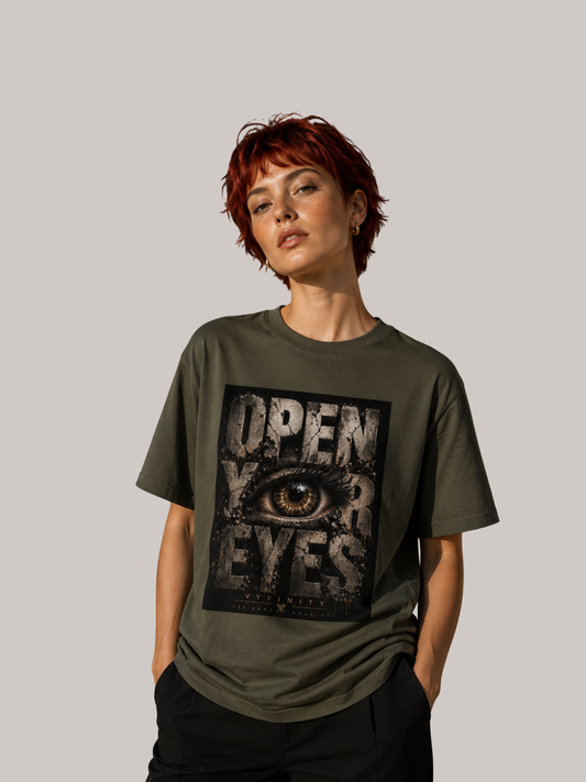 Junge Frau mit kurzen roten Haaren trägt ein olivgrünes VYFINITY Unisex T-Shirt mit großem „OPEN YOUR EYES“-Print und realistischem Auge im markanten Grunge-Design. Moderner Streetwear-Look vor neutralem Studiohintergrund.