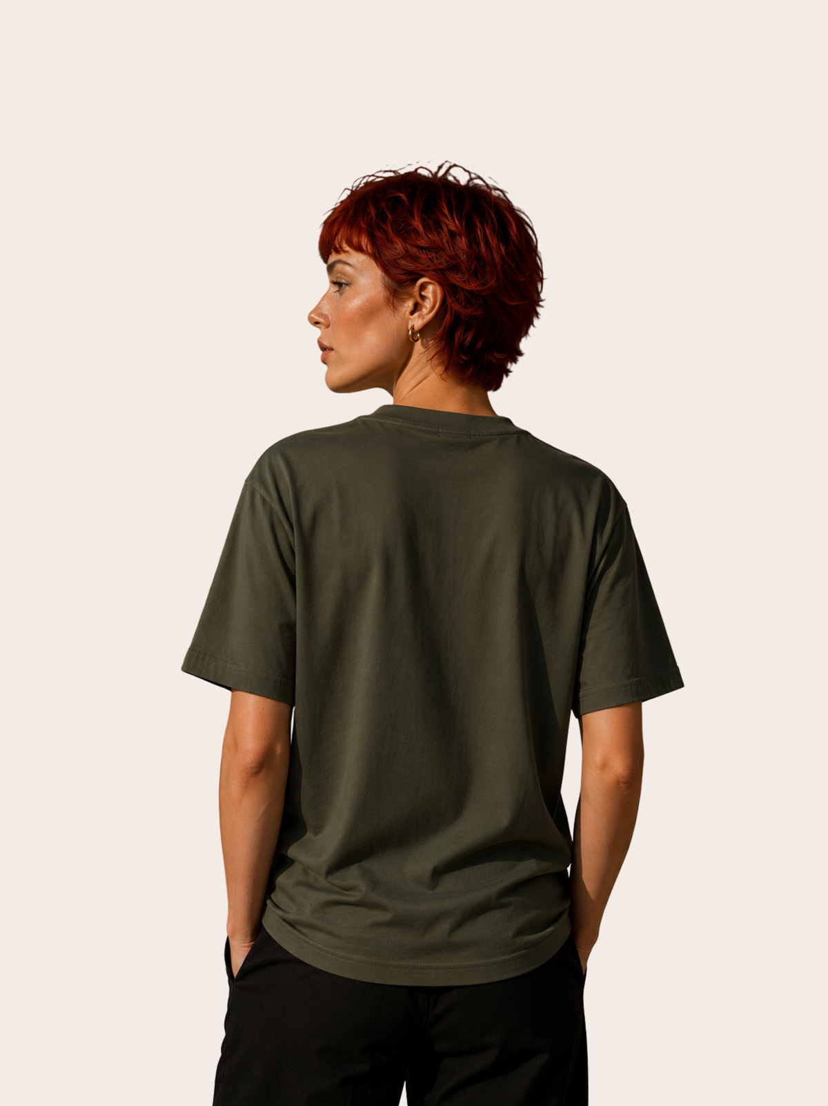  Rückansicht eines weiblichen Models mit kurzem rotem Haar in einem olivgrünen T-Shirt ohne Rückenprint. Das locker geschnittene Shirt wird vor einem hellen, minimalistischen Hintergrund präsentiert.