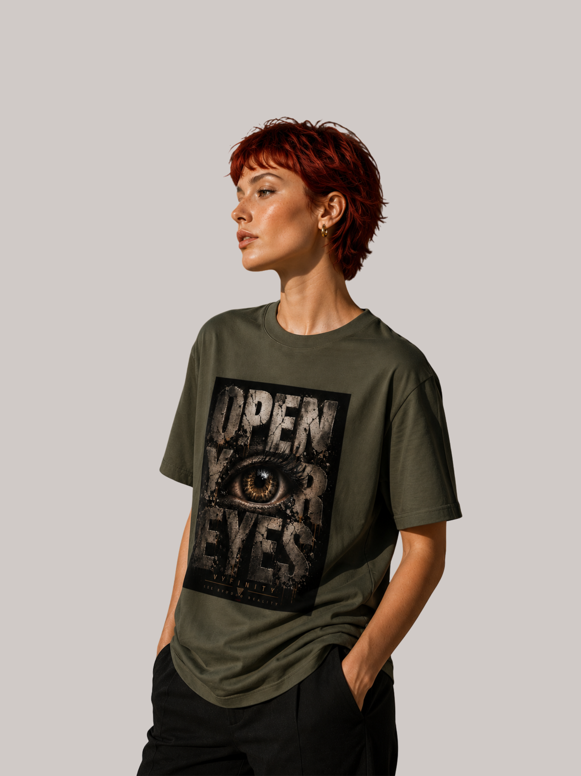 Junge Frau mit kurzen roten Haaren trägt ein olivgrünes VYFINITY Unisex T-Shirt mit großem „OPEN YOUR EYES“-Print und realistischem Auge im markanten Grunge-Design. Seitliche Ansicht im modernen Streetwear-Look vor neutralem Studiohintergrund.