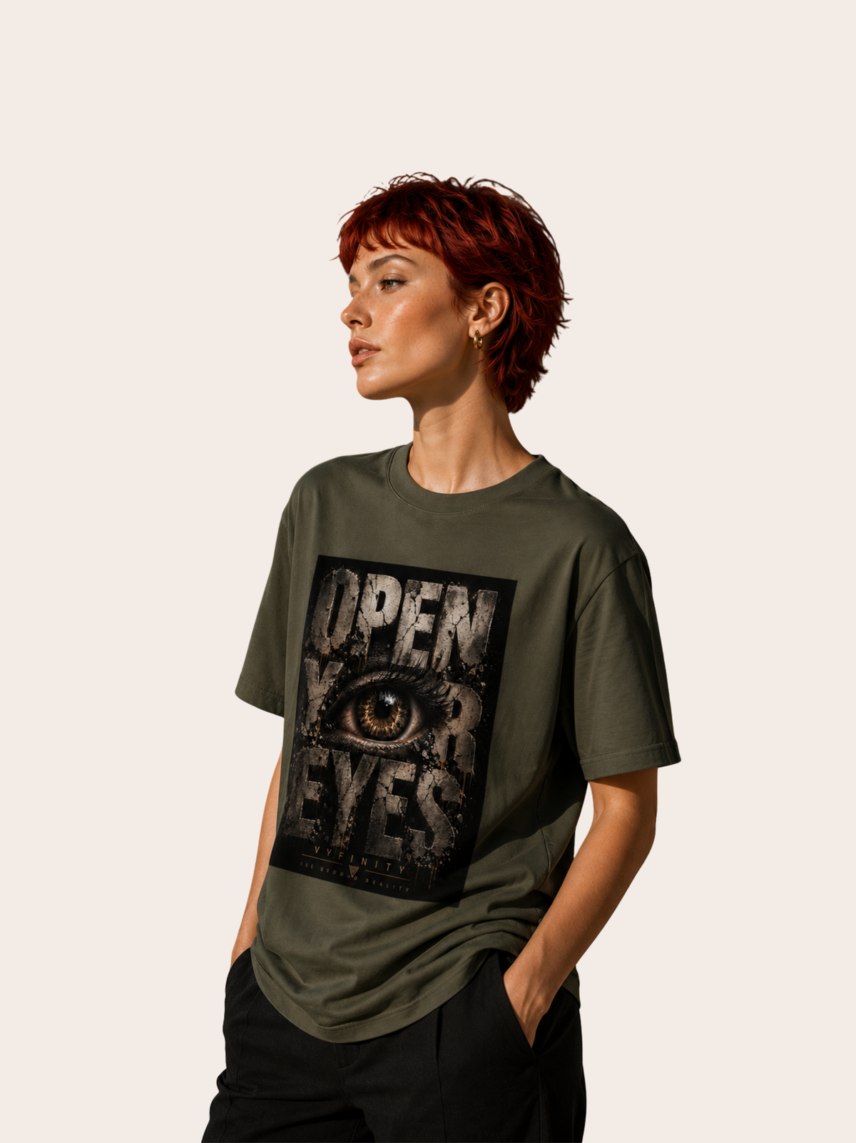 Weibliches Model mit kurzem rotem Haar trägt ein olivgrünes VYFINITY T-Shirt mit großem „OPEN YOUR EYES“-Frontprint. Das markante Grunge-Design zeigt ein detailreiches Auge und VYFINITY-Branding. Das Model steht seitlich vor einem hellen, minimalistischen Hintergrund.