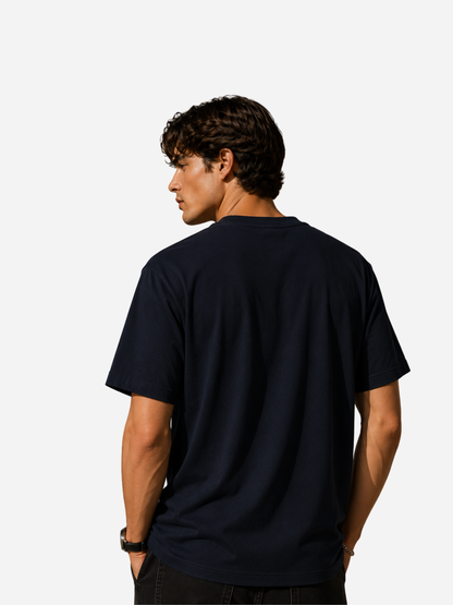 Rückansicht eines jungen Mannes im dunkelblauen Unisex Classic Fit T-Shirt von VYFINITY. Minimalistisches Premium Streetwear-Shirt ohne Frontprint, mit dezentem VYFINITY-Logo im Nacken vor hellem Studiohintergrund.