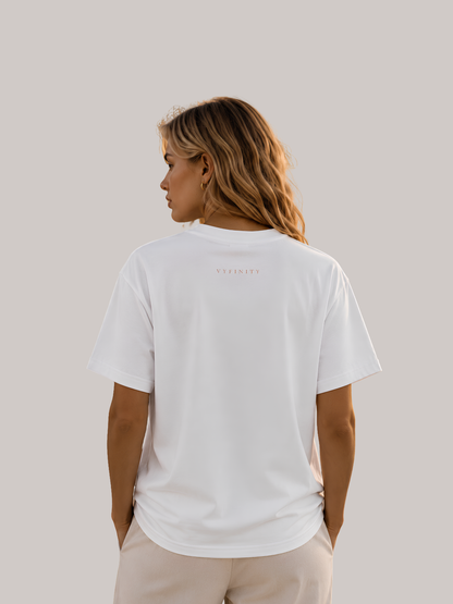 Rückansicht einer blonden Frau mit weißem Unisex Classic Fit T-Shirt im modernen Streetwear-Stil. Minimalistisches Premium Baumwoll-Shirt mit kleinem VYFINITY-Logo im Nackenbereich und zeitlosem Clean-Look für Damen und Herren.