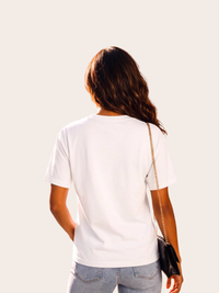 Weibliches Model von hinten in weißem VYFINITY T-Shirt und hellblauer Jeans, kombiniert mit einer kleinen schwarzen Schultertasche mit goldener Kette.