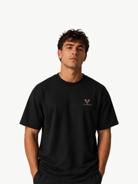 Männliches Model trägt ein schwarzes VYFINITY Heavy T-Shirt in Frontansicht. Auf der linken Brust befindet sich ein kleines VYFINITY-Logo in Weiß und Orange. Cleaner, minimalistischer Premium-Streetwear-Look vor hellem Studiohintergrund.