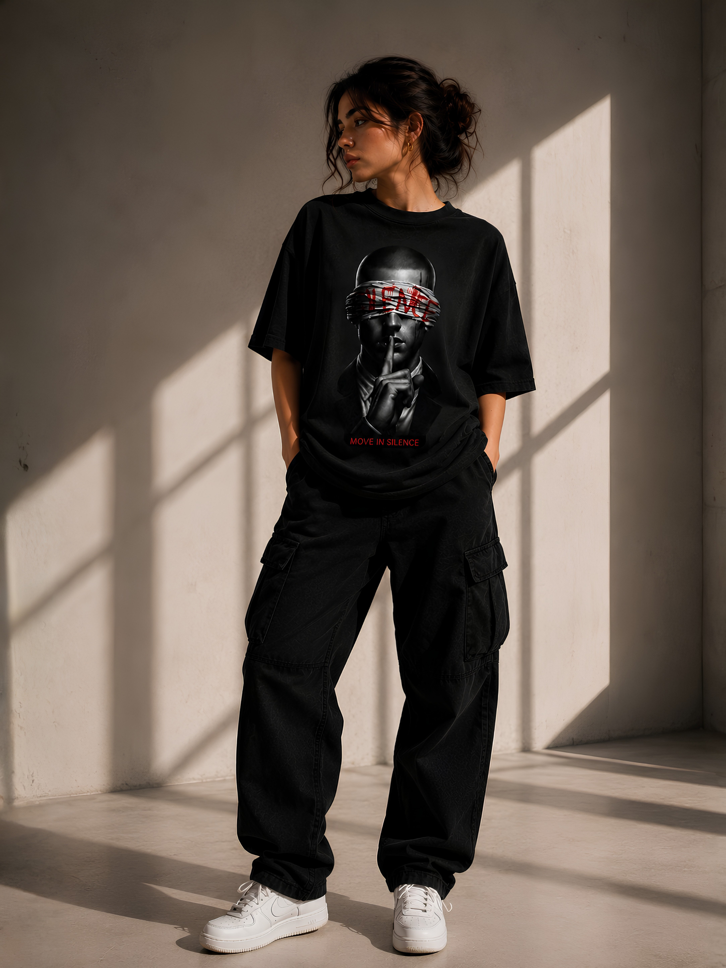Lifestyle-Aufnahme einer Frau mit schwarzem Vyfinity Oversized-T-Shirt. Das Premium-Streetwear-Shirt zeigt einen markanten Frontprint mit einem geheimnisvollen Portrait sowie den Schriftzug „MOVE IN SILENCE“ – moderner Oversized-Look für Damen und Herren.