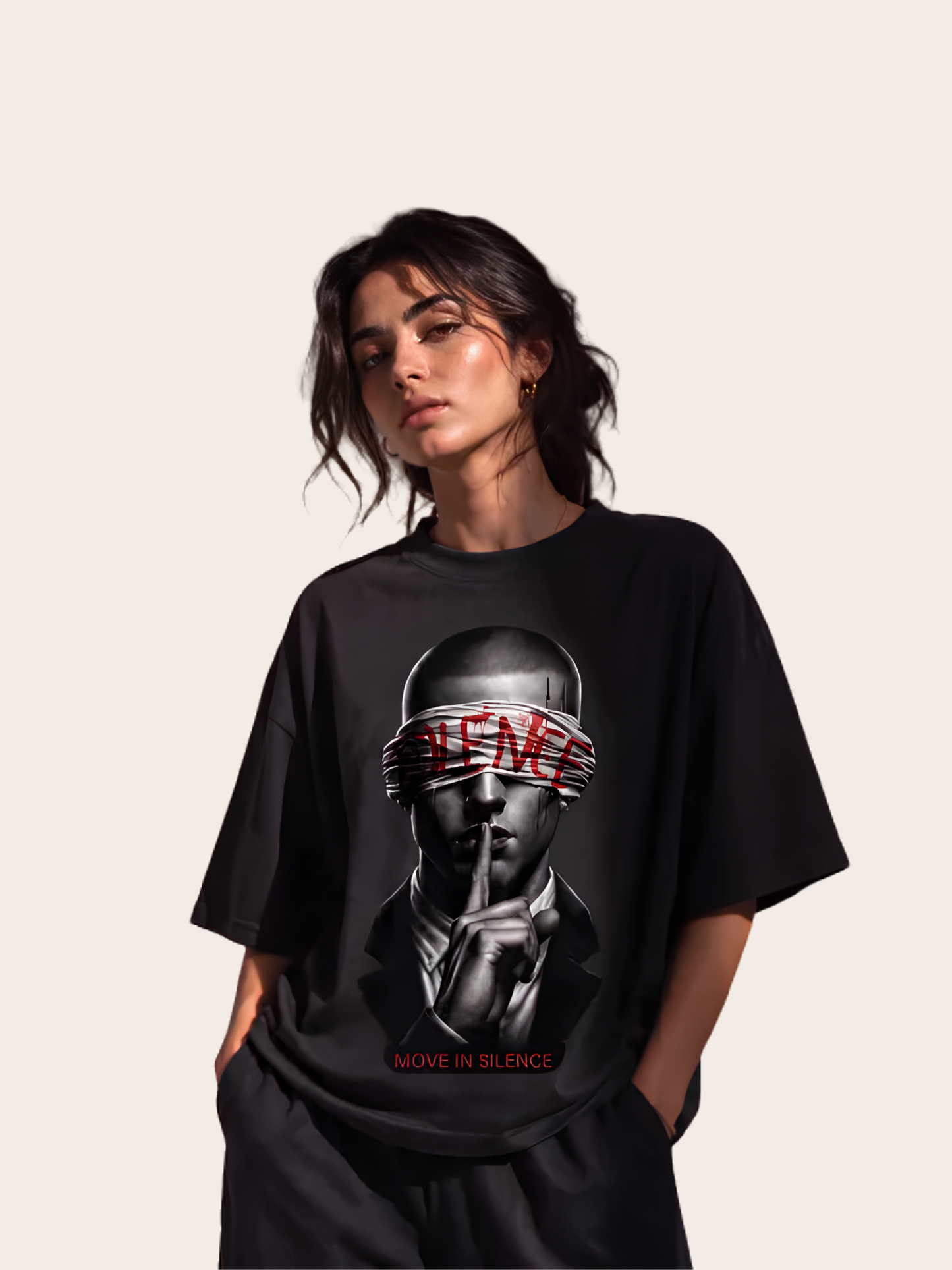 Frau mit dunklen Haaren trägt ein schwarzes Oversized VYFINITY T-Shirt mit großem monochromen Frontprint. Das Motiv zeigt eine stilisierte Person mit verbundenen Augen und Finger vor den Lippen; darunter steht „MOVE IN SILENCE“ in Rot. Modernes schwarzes Streetwear-Outfit vor hellem, neutralem Hintergrund.