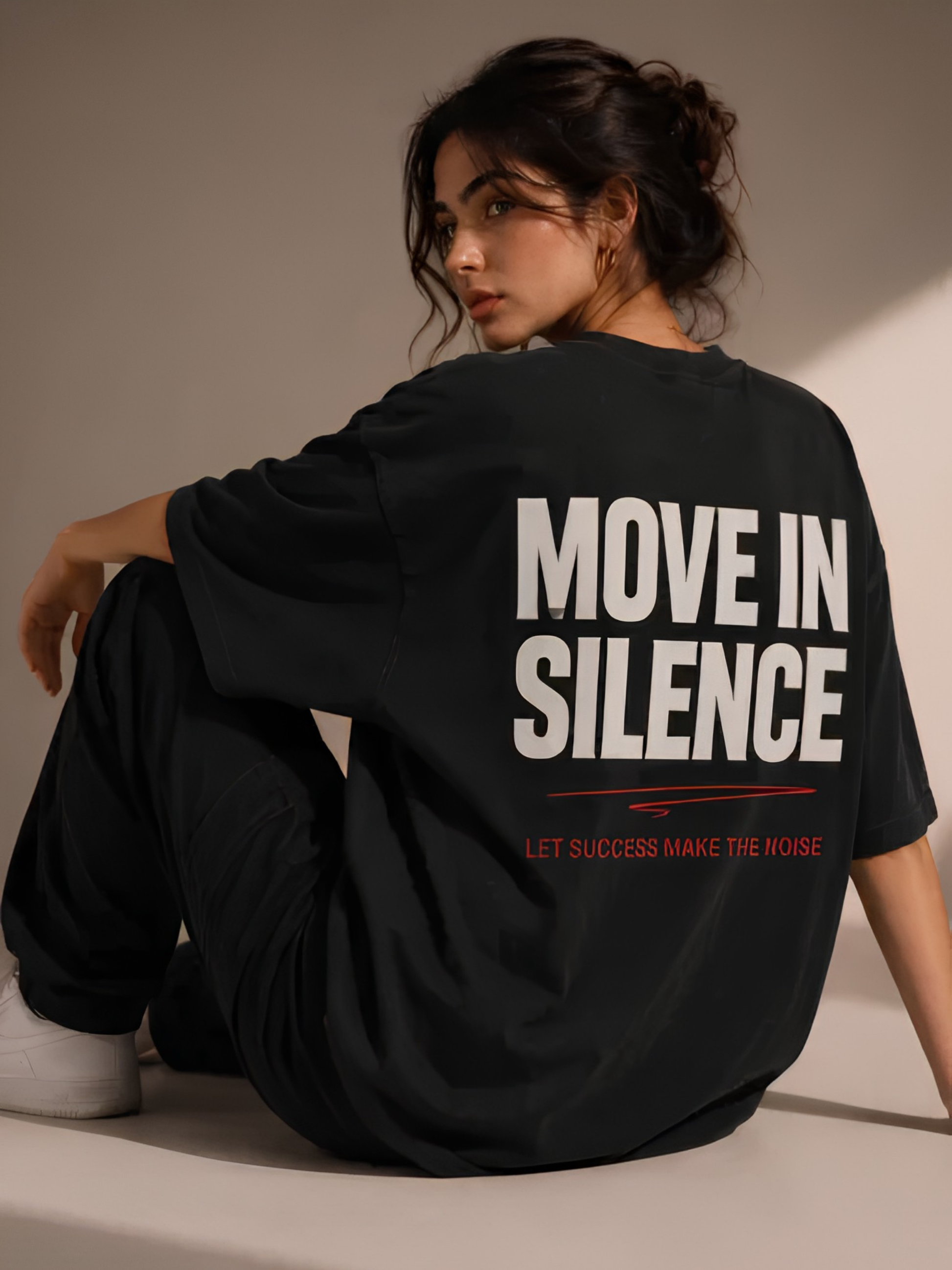 Lifestyle-Aufnahme einer Frau mit schwarzem Vyfinity Oversized-T-Shirt. Der große Rückenprint „MOVE IN SILENCE“ und der rote Schriftzug „LET SUCCESS MAKE THE NOISE“ verleihen dem Premium-Streetwear-Shirt einen modernen Urban-Look.