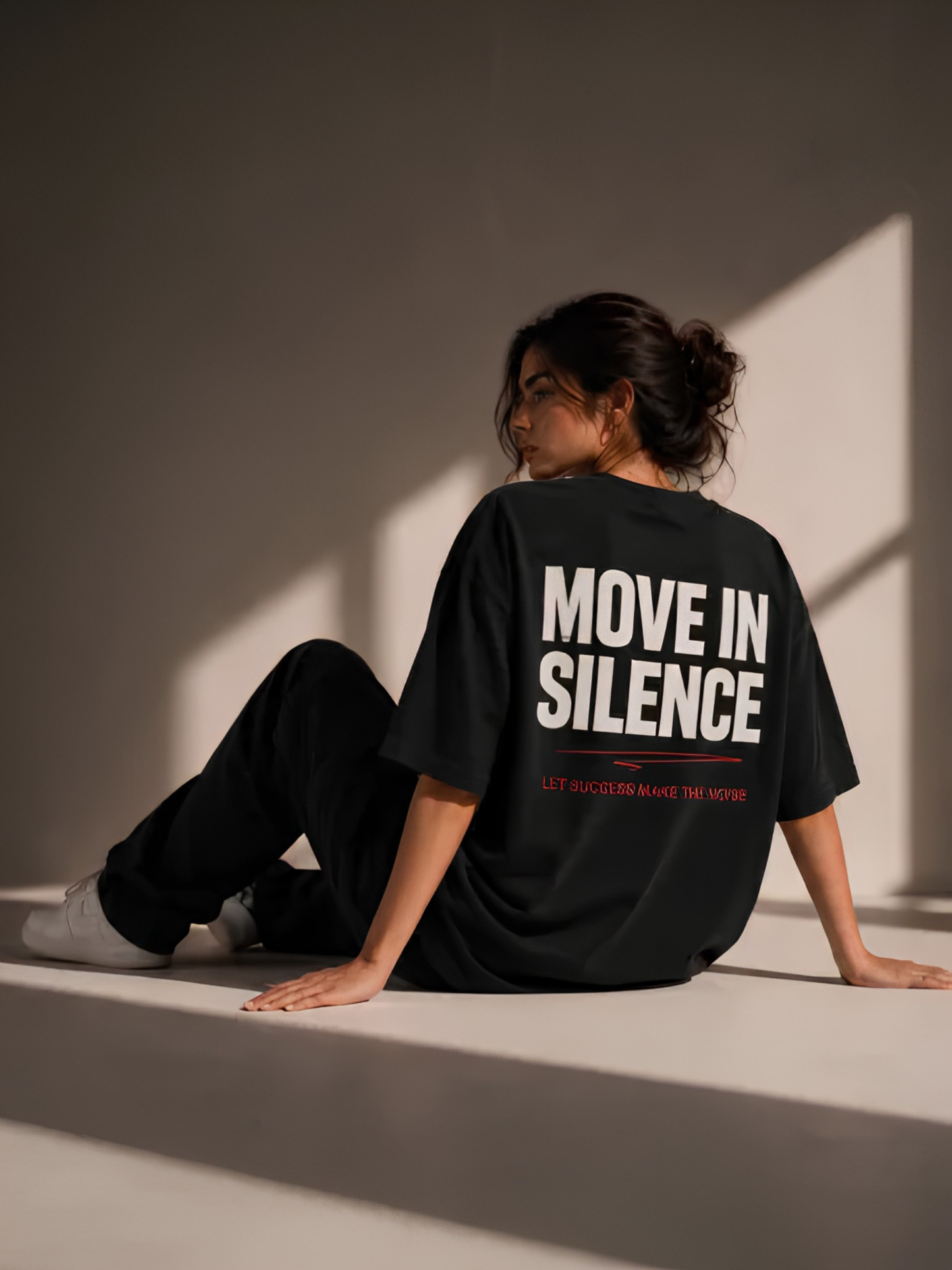 Lifestyle-Aufnahme einer Frau mit schwarzem Vyfinity Oversized-T-Shirt und großem Rückenprint „MOVE IN SILENCE“. Das Premium-Streetwear-Shirt kombiniert minimalistisches Design mit dem roten Statement „LET SUCCESS MAKE THE NOISE“ für einen modernen Urban-Look.