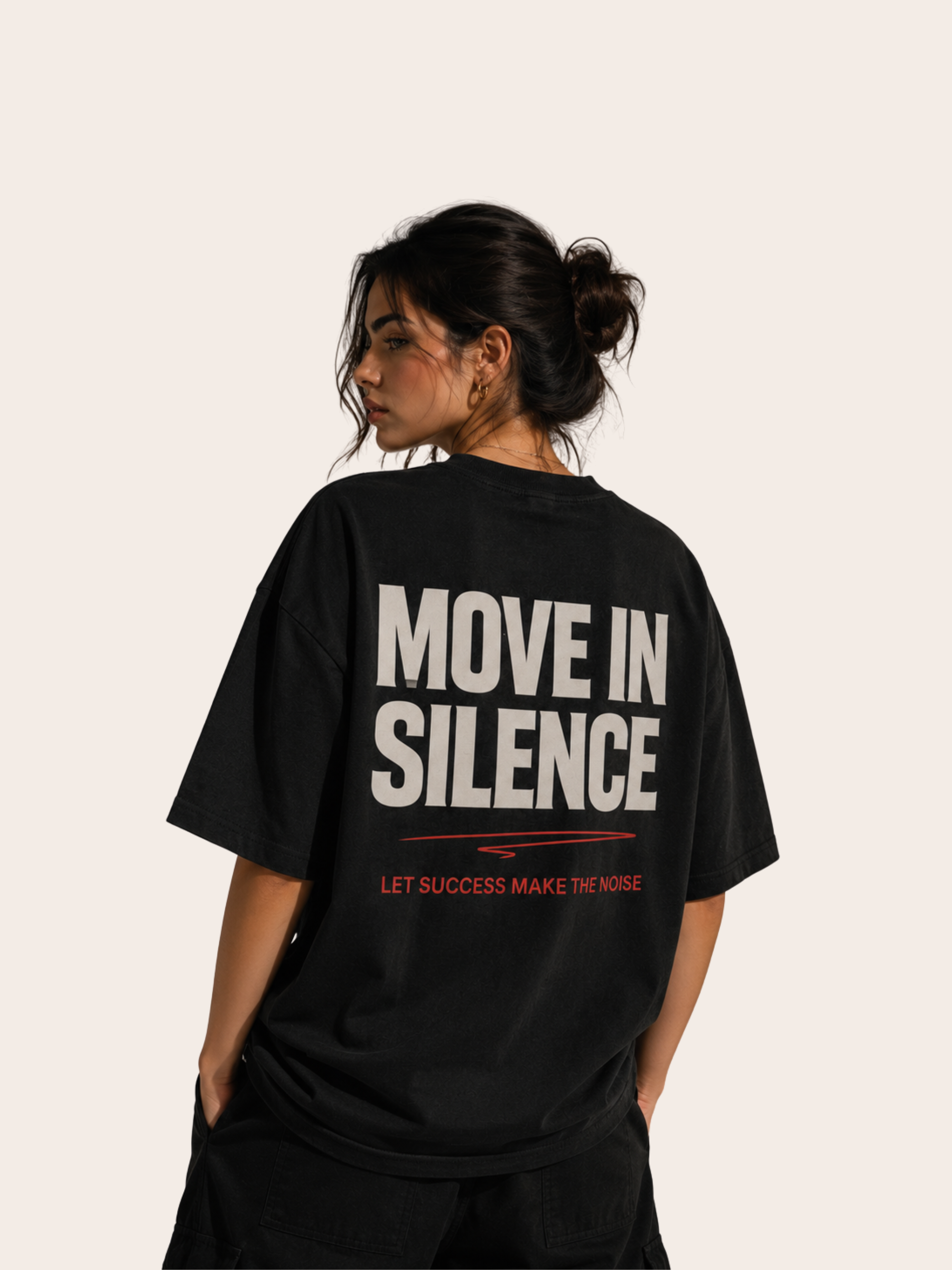 Frau in Rückansicht trägt ein schwarzes Oversized VYFINITY T-Shirt mit großem typografischem Rückenprint „MOVE IN SILENCE“. Darunter stehen rote Akzente und der Schriftzug „LET SUCCESS MAKE THE NOISE“. Moderner minimalistischer Streetwear-Look vor hellem, neutralem Hintergrund.