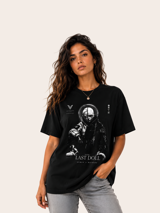 VYFINITY „The Last Doll“ schwarzes T-Shirt mit futuristischem schwarz-weißem Puppen- und Maschinenmotiv, getragen von einem weiblichen Model mit grauer Jeans.