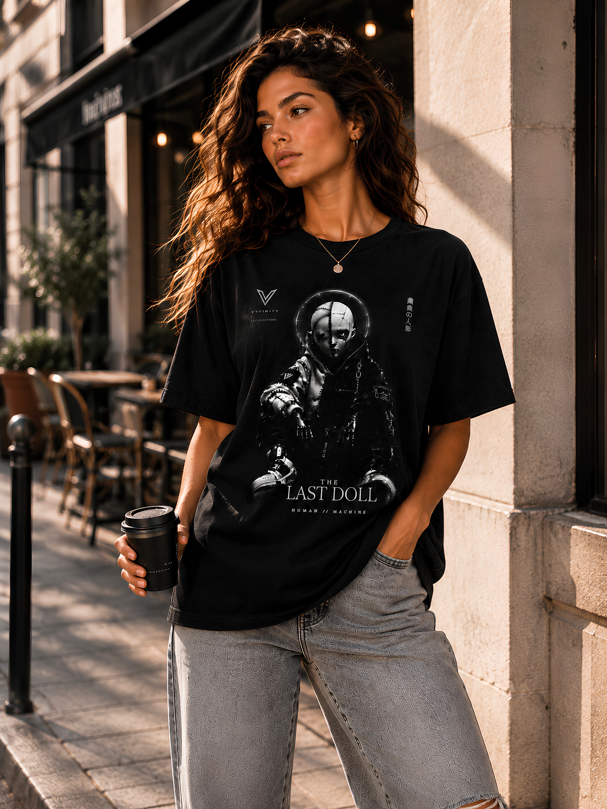 VYFINITY „The Last Doll“ schwarzes Streetwear-T-Shirt an weiblichem Model mit futuristischem Human-Machine-Puppenmotiv, urbanes Lifestyle-Fashion-Shooting vor einem Café.