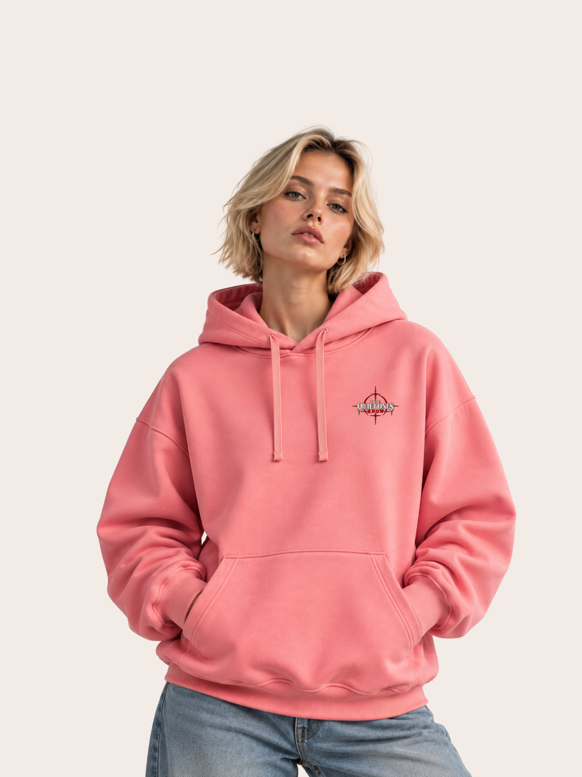 Blondes weibliches Model trägt einen rosa VYFINITY Oversized Hoodie mit kleinem „THE QUIET ONES KNOW“-Brustprint, Kapuze, farblich passenden Kordeln und Kängurutasche.