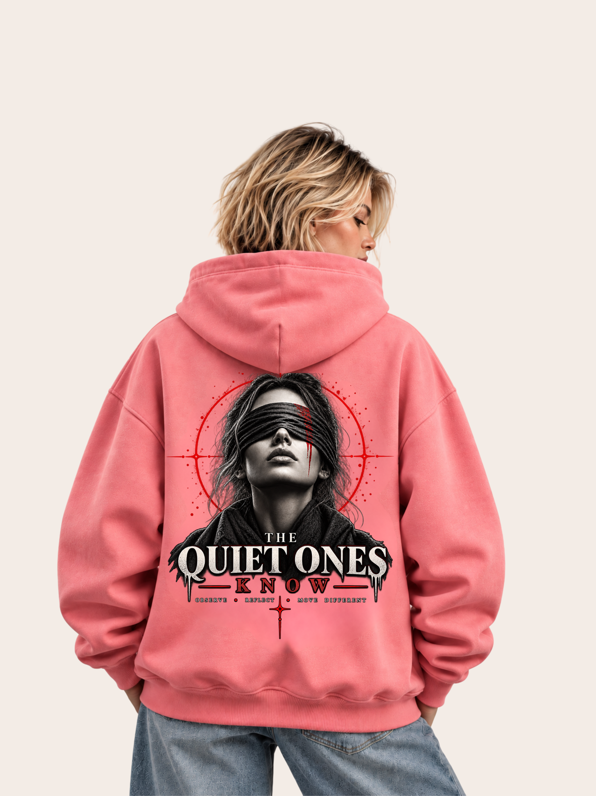 Blondes weibliches Model trägt einen rosa VYFINITY Oversized Hoodie in Rückansicht mit großem „THE QUIET ONES KNOW“-Backprint, schwarz-weißem Frauenporträt mit Augenbinde und markanten roten grafischen Akzenten.