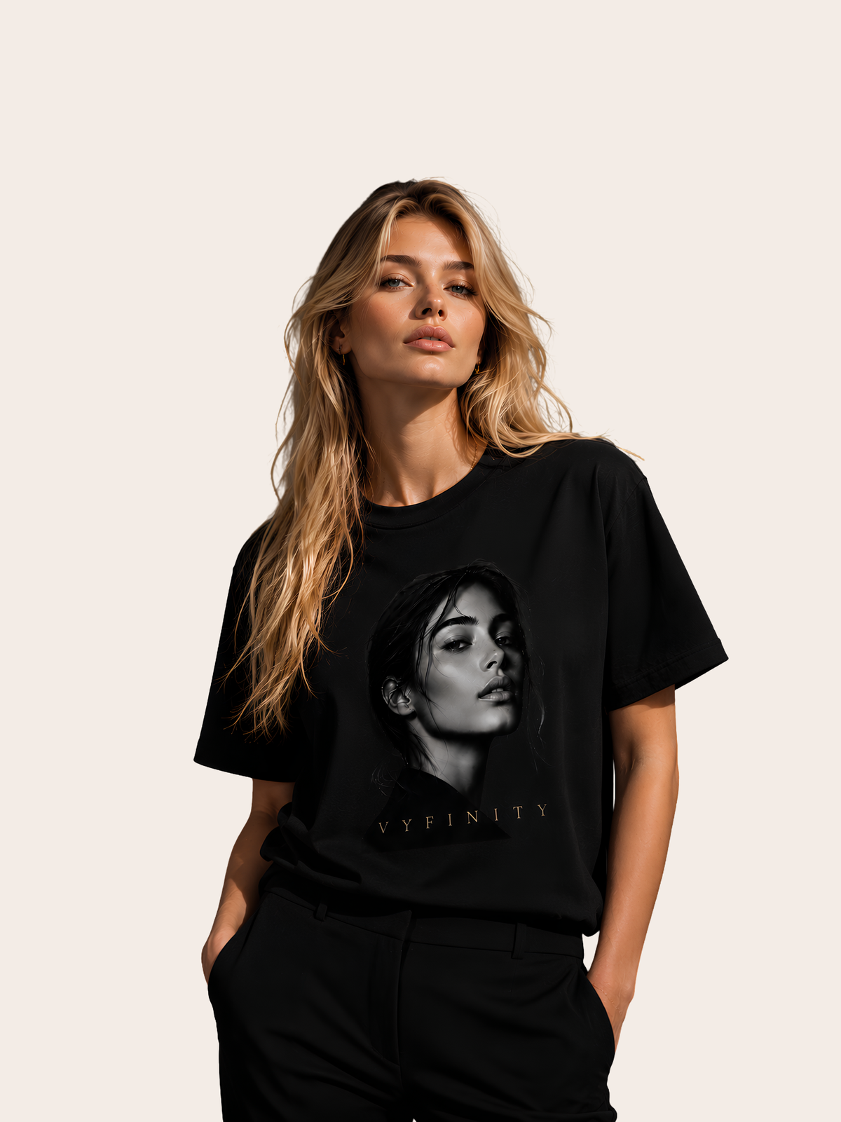 Blonde Frau trägt ein schwarzes VYFINITY T-Shirt mit großem monochromen Frauenporträt und VYFINITY-Schriftzug auf der Vorderseite. Ton-in-Ton schwarzes Outfit vor einem hellen, neutralen Hintergrund – moderner Premium-Streetwear-Look.