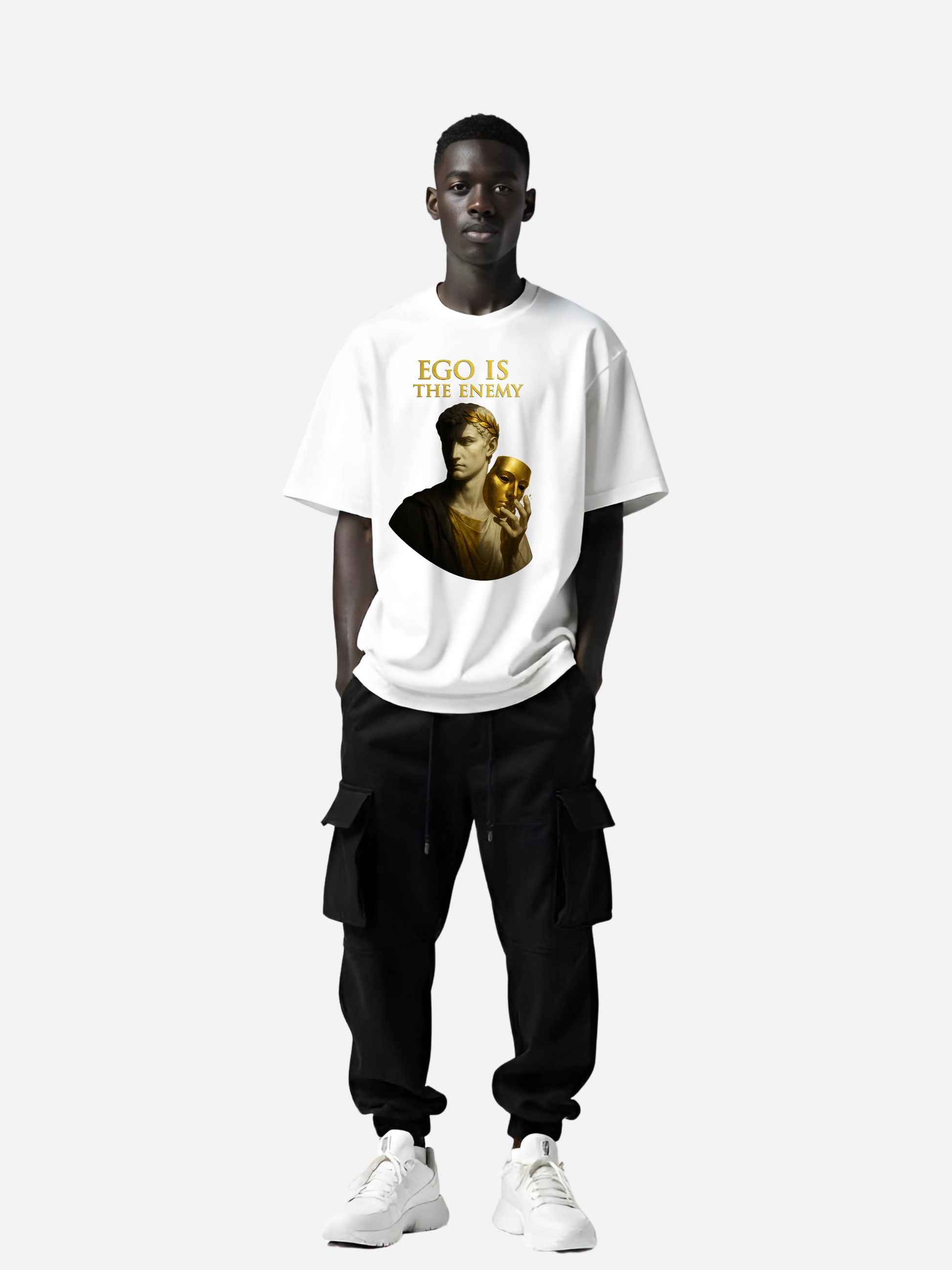 Schwarzer Mann trägt weißes Oversized T-Shirt mit gold-schwarzem Print und Text Ego Is The Enemy, kombiniert mit schwarzer Cargo-Hose und weißen Sneakern